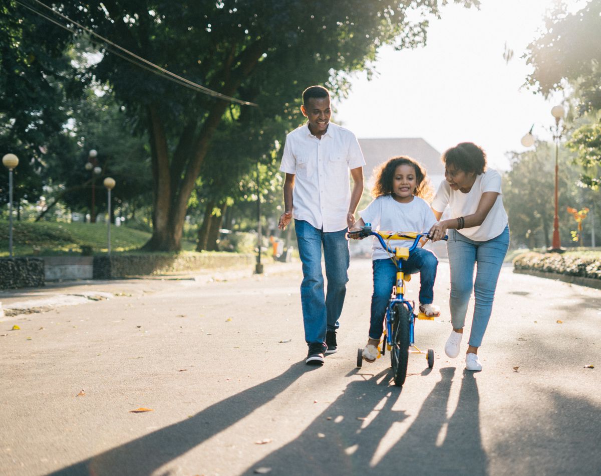 Parents helping a child ride a bicycle outdoors